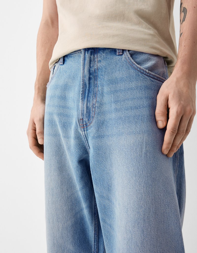 Helle blaue Jeans im Relaxed Fit, mit verblassten Abschnitten, klassischen Taschen und einem dezenten roten Nähakzent.