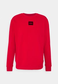 Sudadera de manga larga roja con cuello redondo y parche rectangular negro con la etiqueta "HUGO" centrada en el pecho.