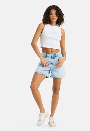 Top court blanc avec un motif vert clair, associé à un short en denim bleu clair. Le mannequin porte des baskets blanches. Design simple et décontracté.