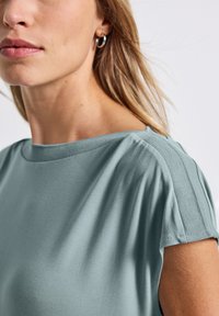 Top azzurro chiaro a maniche corte con una vestibilità morbida, caratterizzato da un colletto tondo e dettagli testurizzati sulle spalle, realizzato in un tessuto morbido e liscio.