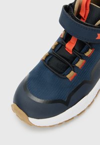 Blue and tan children's sneaker with black elastic laces, orange accents, Velcro strap, and white sole with treaded bottom.