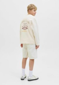 Sudadera de color claro con estampado en la parte trasera, combinada con pantalones cortos a juego. El conjunto presenta un ajuste relajado y un diseño sencillo. Zapatillas con suelas oscuras.