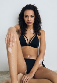 Juodas bikinis su trikampiu viršumi, turinčiu dvi juostas, ir atitinkančiais aukšto liemens apatiniais. Pati tekstūra lygi, su minimaliais akcentais.