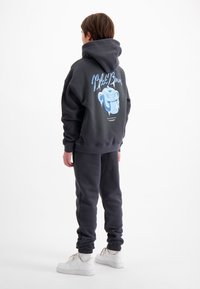 Donkergrijze hoodie en bijpassende broek, met een blauwe grafische afbeelding op de achterkant. Witte sneakers maken de outfit compleet. Zacht, cozy materiaal.