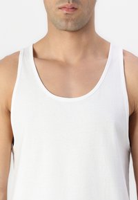 Débardeur en coton blanc avec un col rond et des emmanchures classiques. Texture lisse, design minimaliste, sans motifs ni décorations visibles.