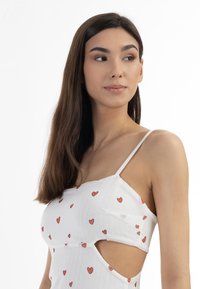 Rochie albă cu bretele subțiri, având un model cu dungi fine și imprimeuri cu inimioare roșii. Include tăieturi pe laterale și o textură netedă.