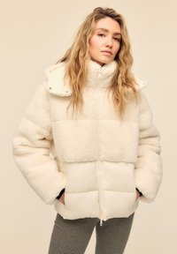 Hvid dunjakke med høj krave, lavet af blødt, tekstureret materiale. Har lynlåslukning og ribkanter; quiltet design på den nederste del.