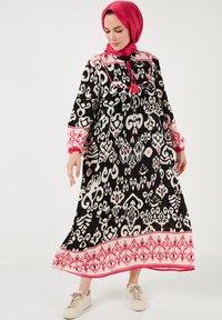 Long black dress featuring white and pink intricate patterns, with pink accents on the collar and cuffs. Paired with light sneakers.