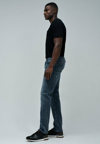 Camiseta negra de manga corta, jeans azules de ajuste slim y zapatillas negras. Diseño simple, sin patrones ni logotipos visibles.
