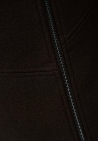 Chaqueta de forro polar marrón oscuro con un prominente zipper plateado en la parte delantera y detalles cosidos en la tela.
