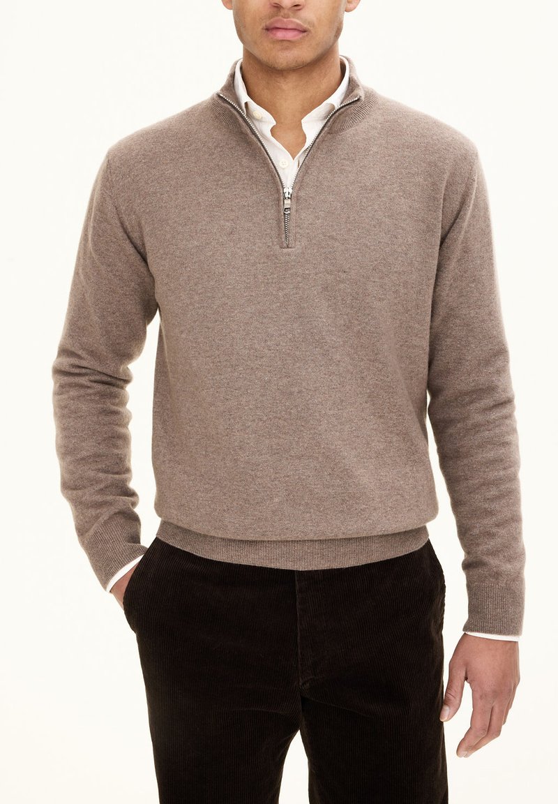 Maglione marrone con zip realizzato in materiale morbido, con colletto alto e polsini a coste, abbinato a pantaloni in velluto a coste scuri.
