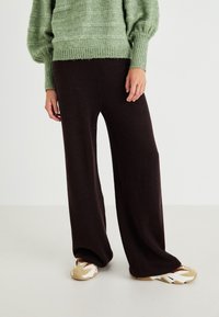 Pantalons larges en maille côtelée marron associés à un pull texturé vert et des baskets beiges avec des accents blancs.