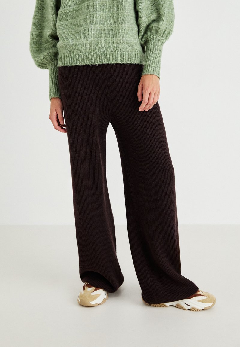 Pantalons larges en maille côtelée marron associés à un pull texturé vert et des baskets beiges avec des accents blancs.