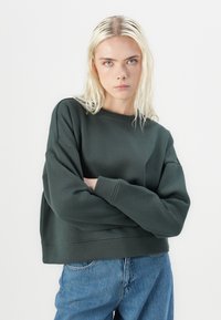 Dark green cropped sweatshirt with a crew neckline, oversized sleeves, and soft texture, paired with light blue high-waisted jeans.