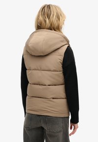 Beige Daunenweste mit Kapuze, horizontal abgesteppt, schwarzen Strickärmeln und subtiler Markenkennzeichnung auf dem Rücken.