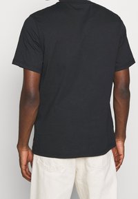 Černé bavlněné tričko s krátkým rukávem, kulatým výstřihem a volným střihem. Obsahuje rovný lem a jemné stehování na manžetách.