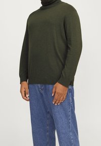 Ciemnozielony sweter z golfem wykonany z miękkiego dzianinowego materiału, z długimi rękawami i prążkowanym kołnierzem, w zestawie z jasnoniebieskimi dżinsami.