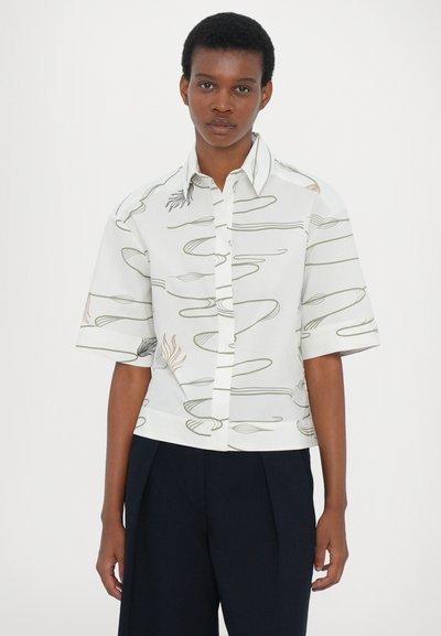 Short-sleeve white shirt with green and brown abstract line patterns, button-down front, and straight-cut hem. Smooth fabric texture.
