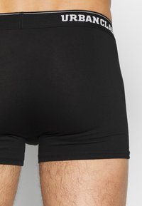 Schwarze Baumwoll-Boxershorts in enger Passform, mit einem breiten, elastischen Bund, der in Weiß mit "URBANCLASSIC" beschriftet ist. Glatte Textur.