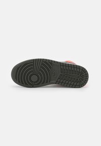 Semelle en caoutchouc noir d'une basket Nike montrant des motifs circulaires et en quadrillage avec le logo Nike au centre, chaussure positionnée semelle vers le haut sur fond blanc.