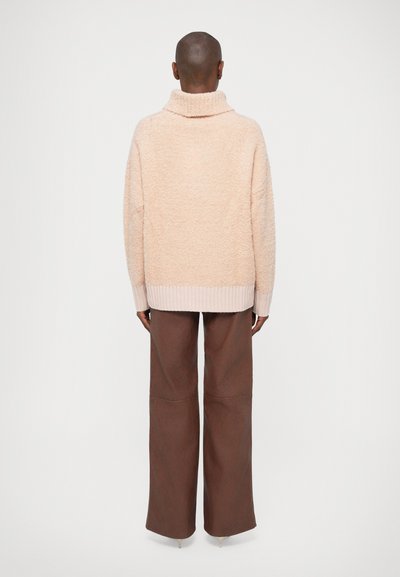 Maglione oversize di colore rosa chiaro, morbido e peloso, con colletto alto e orlo a coste. Abbinato a pantaloni larghi marroni con dettagli nelle cuciture.