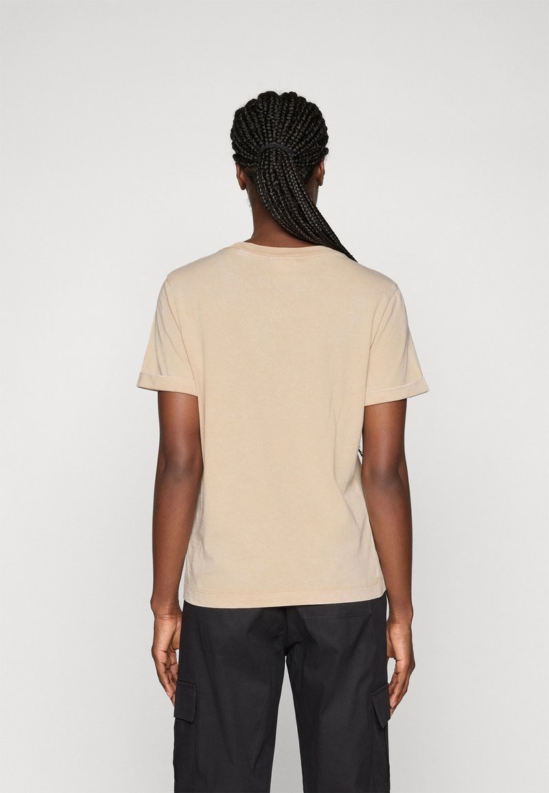 Beige Baumwoll-T-Shirt mit kurzen Ärmeln, hat einen lässigen Schnitt und umgeschlagene Ärmelabschlüsse. Glatte Textur, einfaches Design, keine Muster.