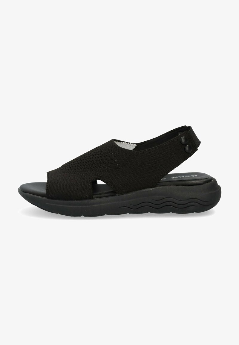 Sandale noire à bout ouvert avec dessus en tricot, semelle rembourrée, bride de talon ajustable avec deux boutons, et semelle extérieure texturée ondulée.
