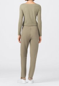 Olivgrünes Langarmshirt kombiniert mit passenden tapered Pants. Weicher Stoff mit glatter Textur, abgerundet mit weißen Sneakers.