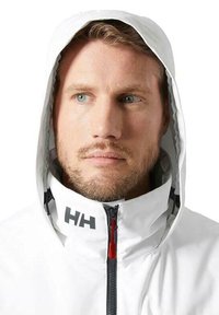 Chaqueta blanca impermeable con capucha, con cremallera y logo gris. Tejido texturizado con acento rojo en la cremallera.