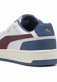 Hvide sneakers med burgunder og blå accenter. Har en tekstureret læderoverdel, polstret krave og en tyk hvid sål med "PUMA" præget.