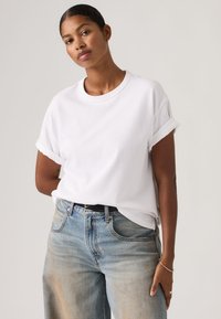 Λευκό βαμβακερό T-shirt με γυρισμένα μανίκια, σε συνδυασμό με ξεθωριασμένο ανοιχτό μπλε τζιν. Απλός σχεδιασμός, άνετη εφαρμογή και απαλή υφή. Μινιμαλιστικό στυλ.