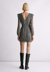 Vestido mini con estampado floral, con espalda en V y mangas largas transparentes, presenta fruncidos y una silueta ajustada, combinado con botas negras hasta la rodilla.