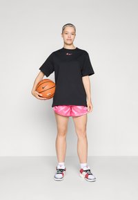 Black oversized t-shirt, pink logo, pink satin shorts, basketball in one hand, detailed white and red sneakers, neutral background.