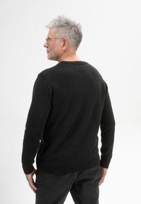 Zwarte gebreide trui met een ronde hals, geribbelde mouwen en onderkant. Glad textuur, aansluitend ontwerp en subtiele details op de schouders.