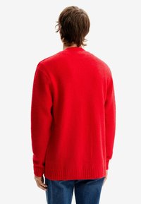 Maglione rosso lavorato a maglia con finitura texturizzata e polsini e orlo a costine, caratterizzato da una vestibilità rilassata e scollatura rotonda. Visto da dietro.
