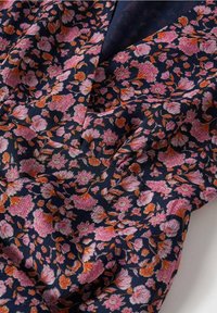 Tissu à motif floral présentant des fleurs roses et orange sur un fond bleu marine, avec une texture plissée et un drapé fluide.