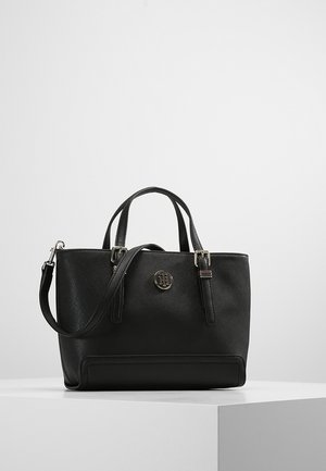 Schwarze, strukturierte Handtasche mit zwei Griffen und verstellbarem Schulterriemen, mit rundem Metall-Logoemblem mittig vorne.