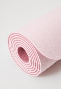 Tapis de yoga rose enroulé, présentant un motif texturé de feuilles, avec une surface lisse et une couleur intérieure contrastante, affichant une forme circulaire.