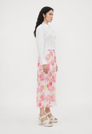 Weißes, kurzes Hemd mit strukturierten Details, kombiniert mit einem langen, fließenden Rock mit abstrakten Mustern in Rosa und Gelb. Chunky-Heels.