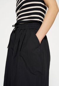 Zwarte lichtgewicht broek met een elastische tailleband, trekkoorddetail en zijzakken. Kenmerkt zich door een subtiele geborduurde logo nabij de zak.