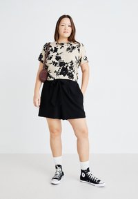 Camiseta beige con estampado floral combinada con pantalones cortos negros con cintura de lazo, complementada con zapatillas negras de caña alta y calcetines blancos.