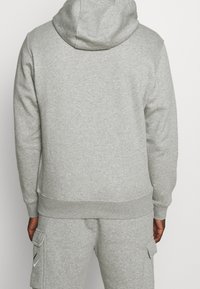 Sudadera gris hecha de material suave, con capucha, dobladillo acanalado y costura lateral. Combinada con pantalones cargo a juego.