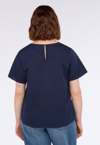Blusa blu navy a maniche corte con dettaglio di apertura a chiave sul retro, realizzata in tessuto liscio. Presenta una vestibilità ampia e un collo arrotondato.