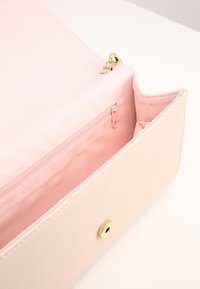 Ljusrosa väska med en slät yta, utrustad med ett guldklämt lås och en inre dragkedja. Enkel, rektangulär design.