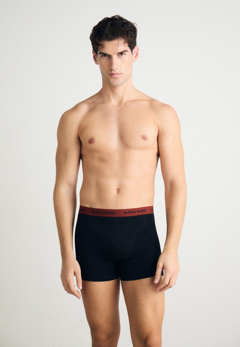 Black boxer briefs with a red elastic waistband featuring the brand name "BJÖRN BORG." Smooth fabric, fitted design, and mid-thigh length.