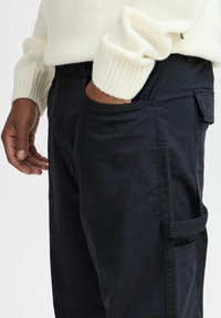 Black cargo pants with a smooth texture, featuring side pockets and a relaxed fit, paired with a cream-colored ribbed knit sweater.