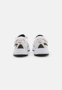Scarpe sportive bianche con una tomaia in mesh traspirante, accenti neri e dorati, colli imbottiti e suole in gomma testurizzata.