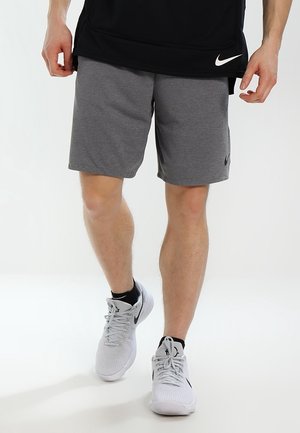Personne portant un short Nike gris, un t-shirt Nike noir, des baskets Nike blanches et des chaussettes noires marchant sur fond blanc.