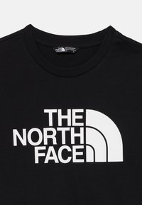 Μαύρο βαμβακερό T-shirt με έντονο λευκό λογότυπο που γράφει "THE NORTH FACE" και καμπυλωτό γραφικό σχέδιο. Στρογγυλή λαιμόκοψη.