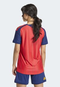 Red and blue sports jersey features horizontal stripes, short sleeves, and a round neckline, paired with blue shorts and yellow accents.
